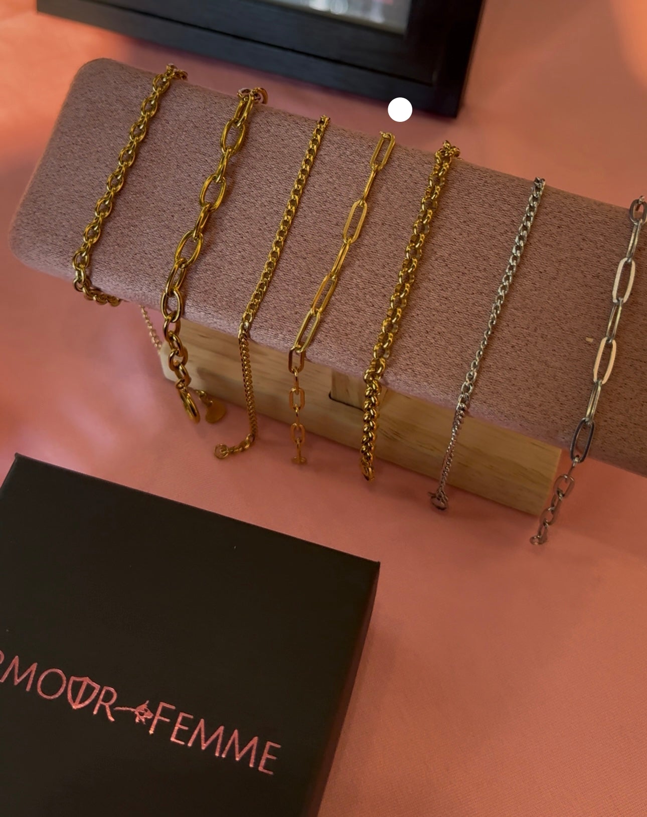 Set of gold and silver chains on a wooden block with 'AMOUR FEMME' branding.