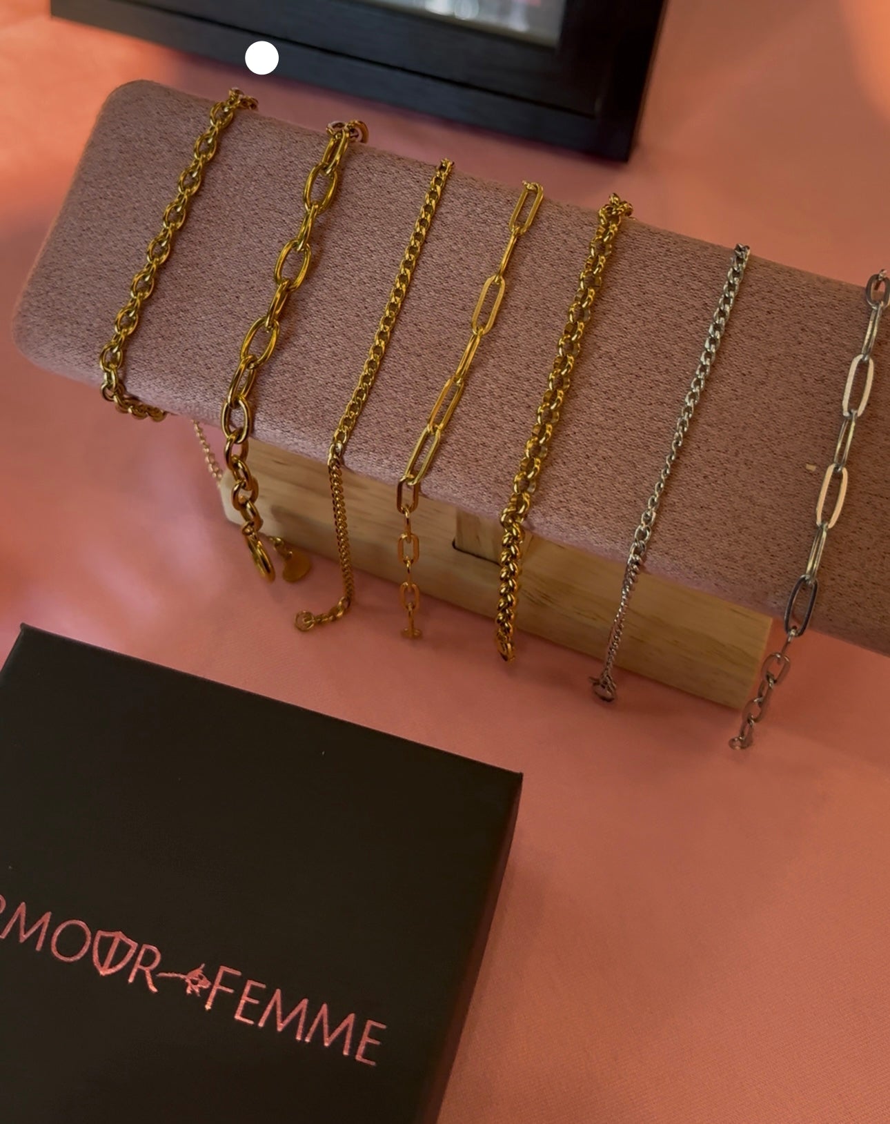 Set of gold and silver chains on a wooden block with 'AMOUR FEMME' branding.