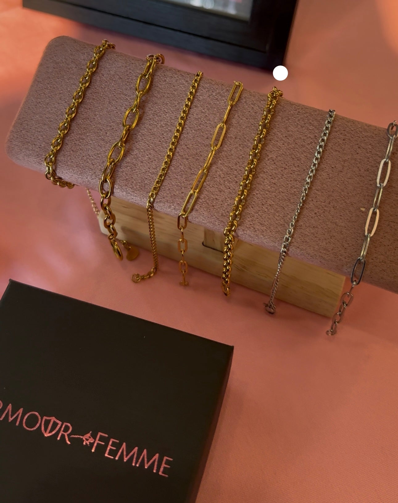 Set of gold and silver chains on a wooden block with 'AMOUR FEMME' branding.